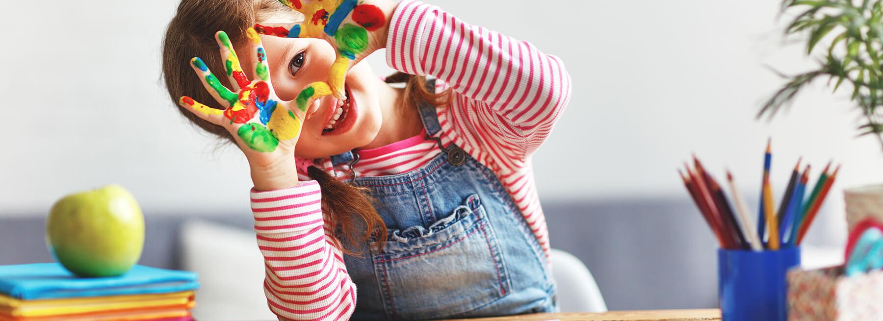 A child smiling through her brightly painted hands