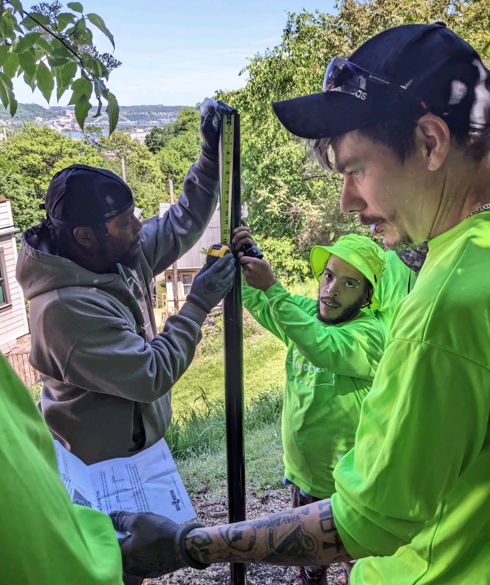 Crew members in bright green shirts check a plan sheet while setting a tall metal post on a hillside