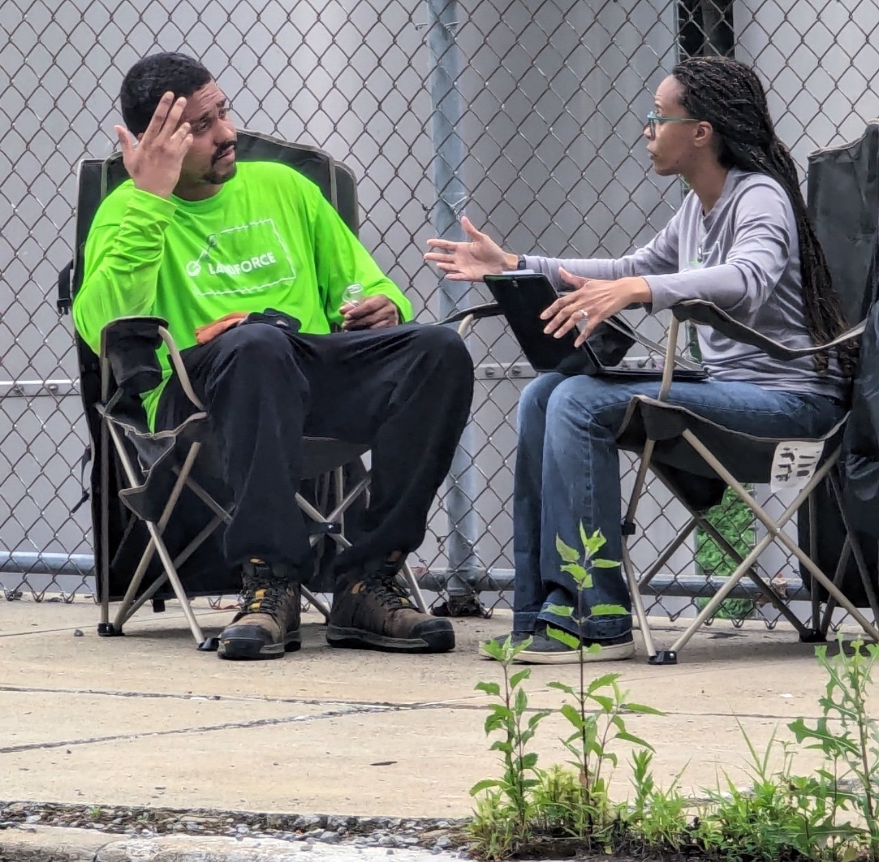 A crew member in a green Landforce shirt and a staff member with a clipboard talk one-on-one in camp chairs