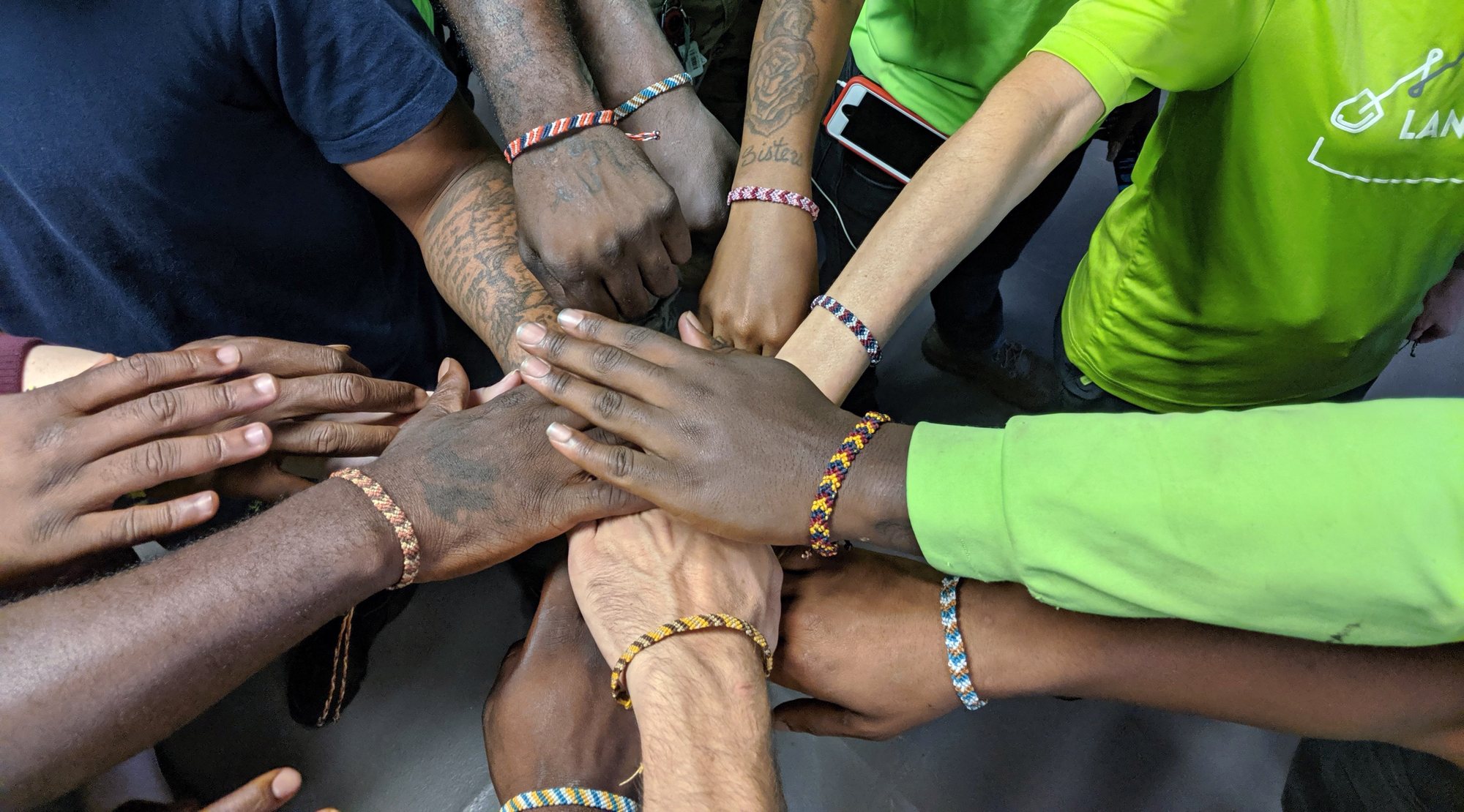 Crew members, several in bright green shirts, stack their hands together in a circle