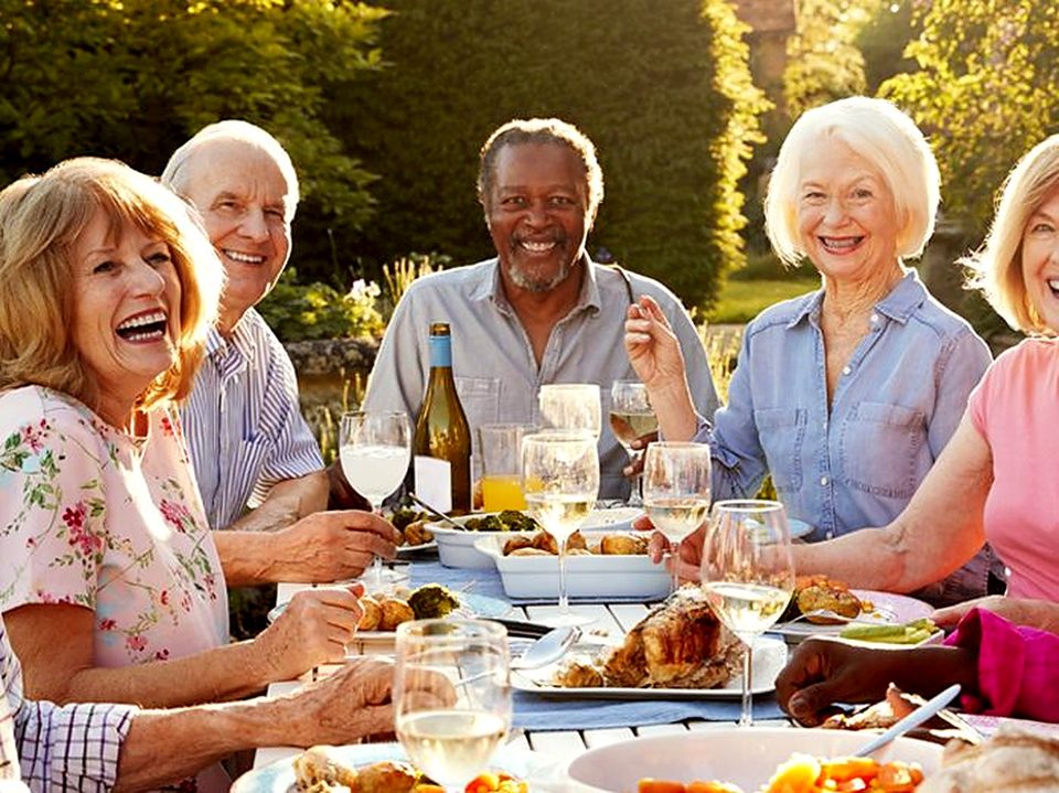 Older friends laughing over lunch at an outdoor table