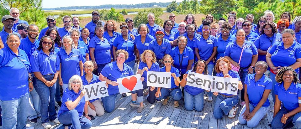 Senior Services staff in blue shirts holding signs that read We love our seniors