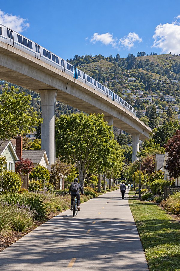 The elevated BART viaduct over the Ohlone Greenway in El Cerrito, a train crossing above people walking and cycling the path below